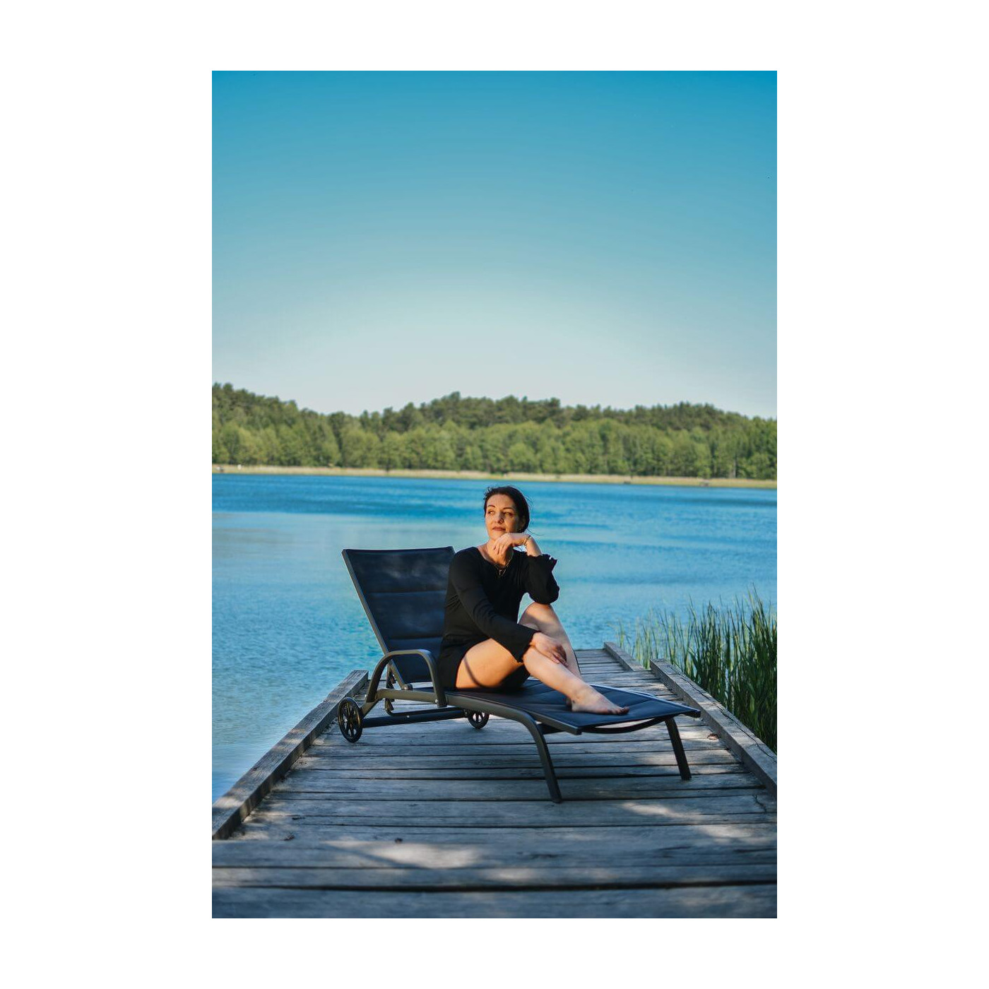 Kobieta siedząca na leżaku na pomoście na tle jeziora i niebieskiego nieba