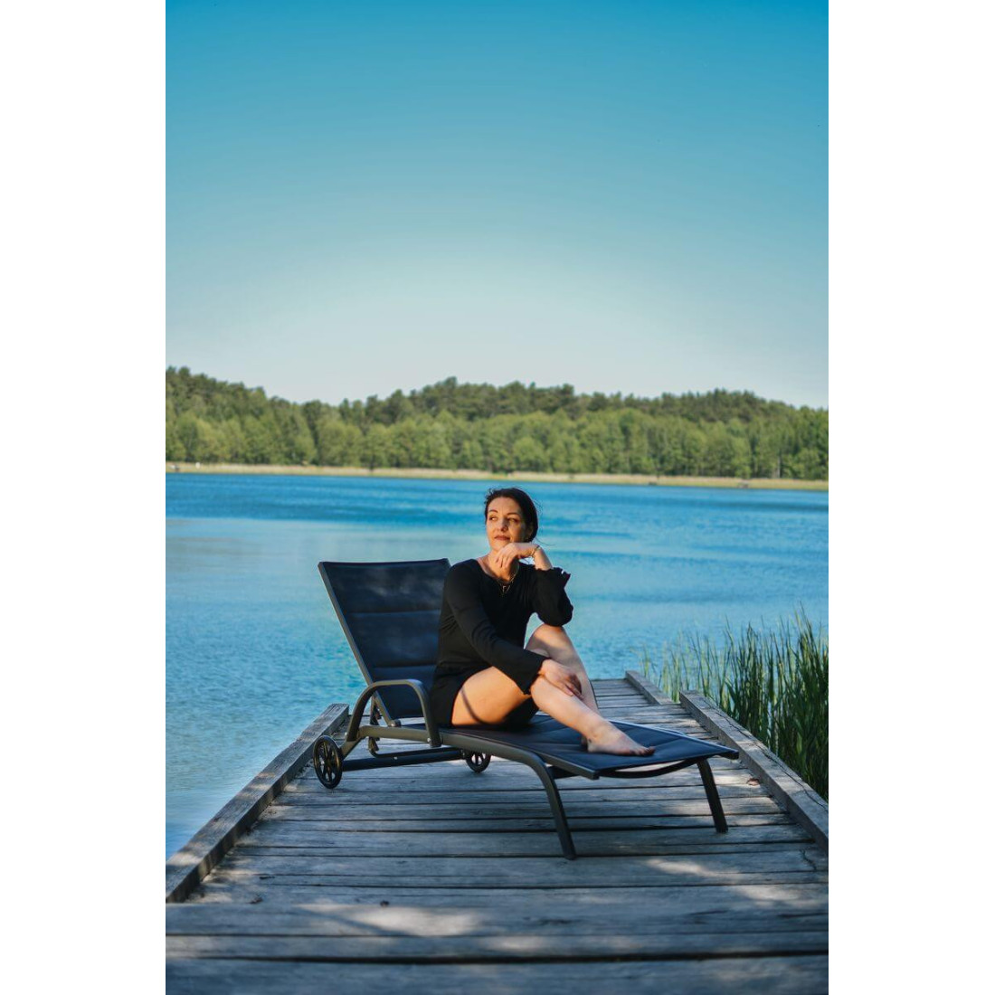Kobieta siedząca na leżaku na pomoście na tle jeziora i niebieskiego nieba