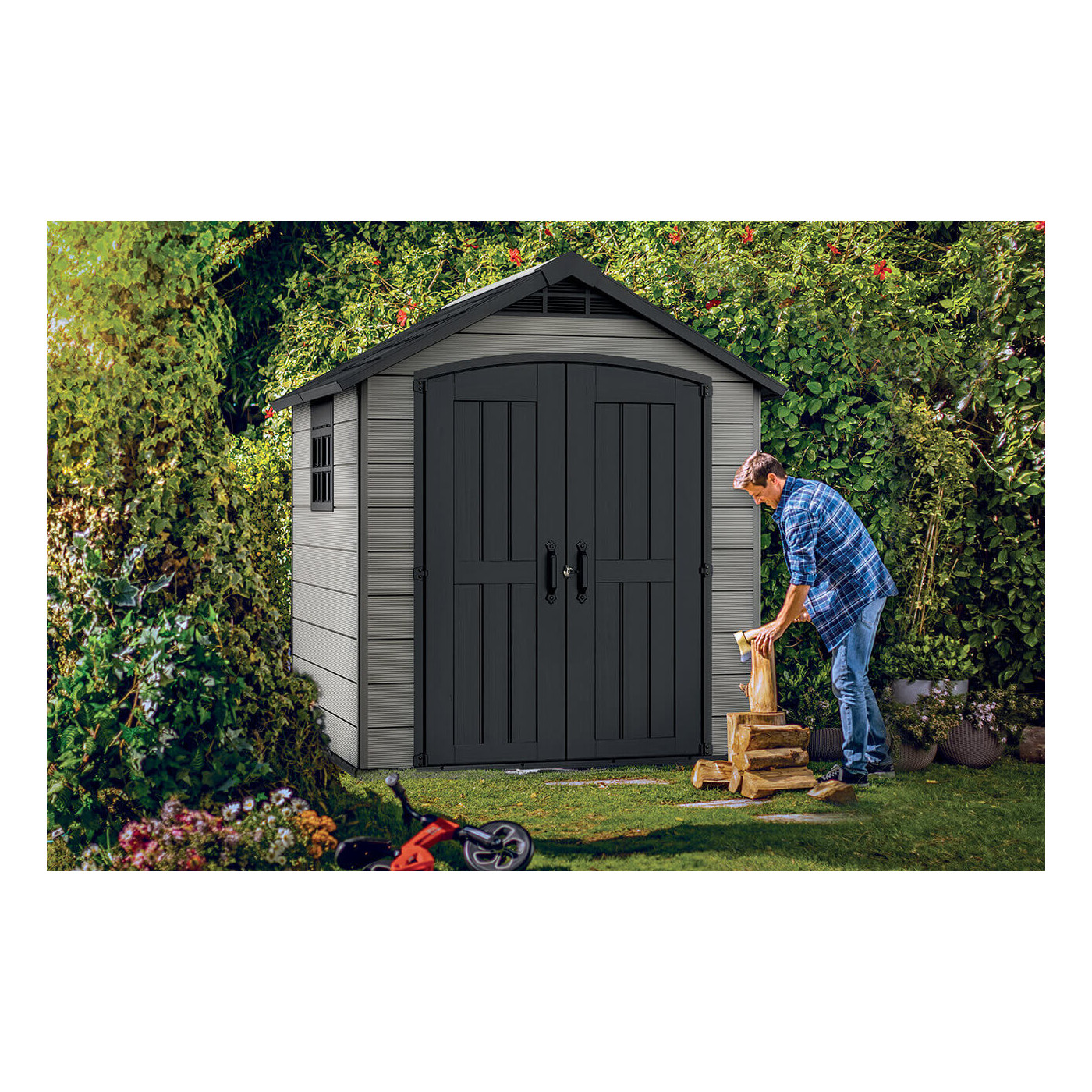 Na pierwszym planie mężczyzna rąbiący drewno, a za nim domek narzędziowy Premier 757 od firmy Keter