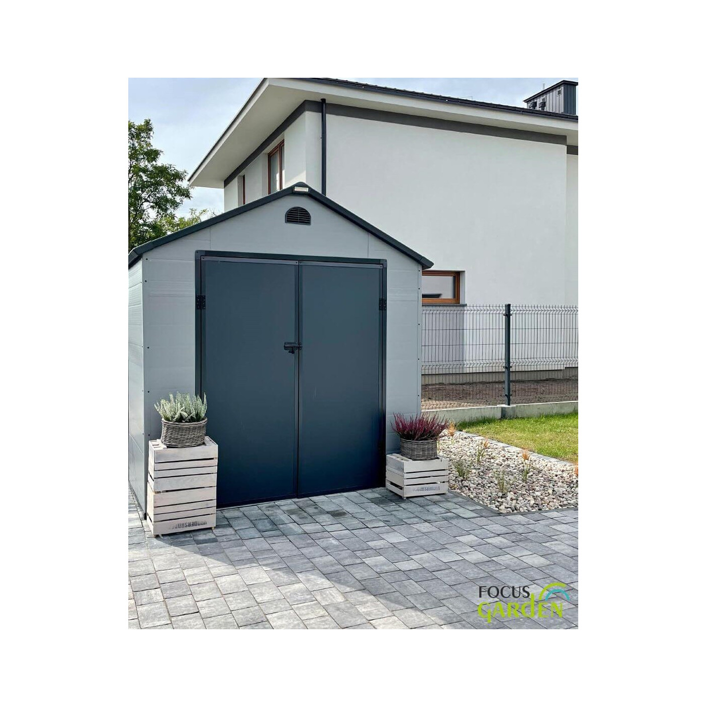 Aranżacja w ogrodzie domku narzędziowego Vermont 242x192cm od Hardmaister, kwiaty stoją przed domkiem, zabudowania za domkiem