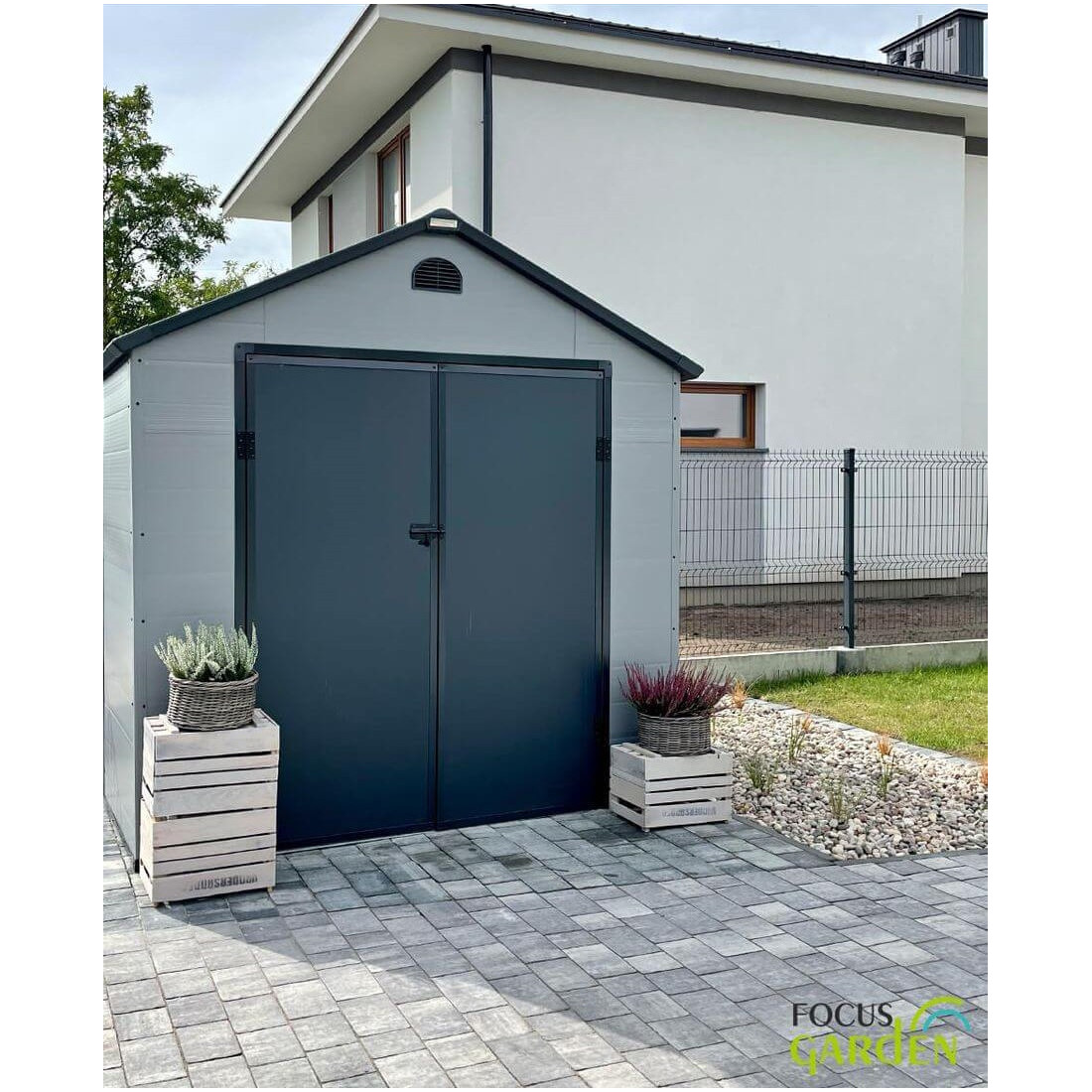 Aranżacja w ogrodzie domku narzędziowego Vermont 242x192cm od Hardmaister, kwiaty stoją przed domkiem, zabudowania za domkiem