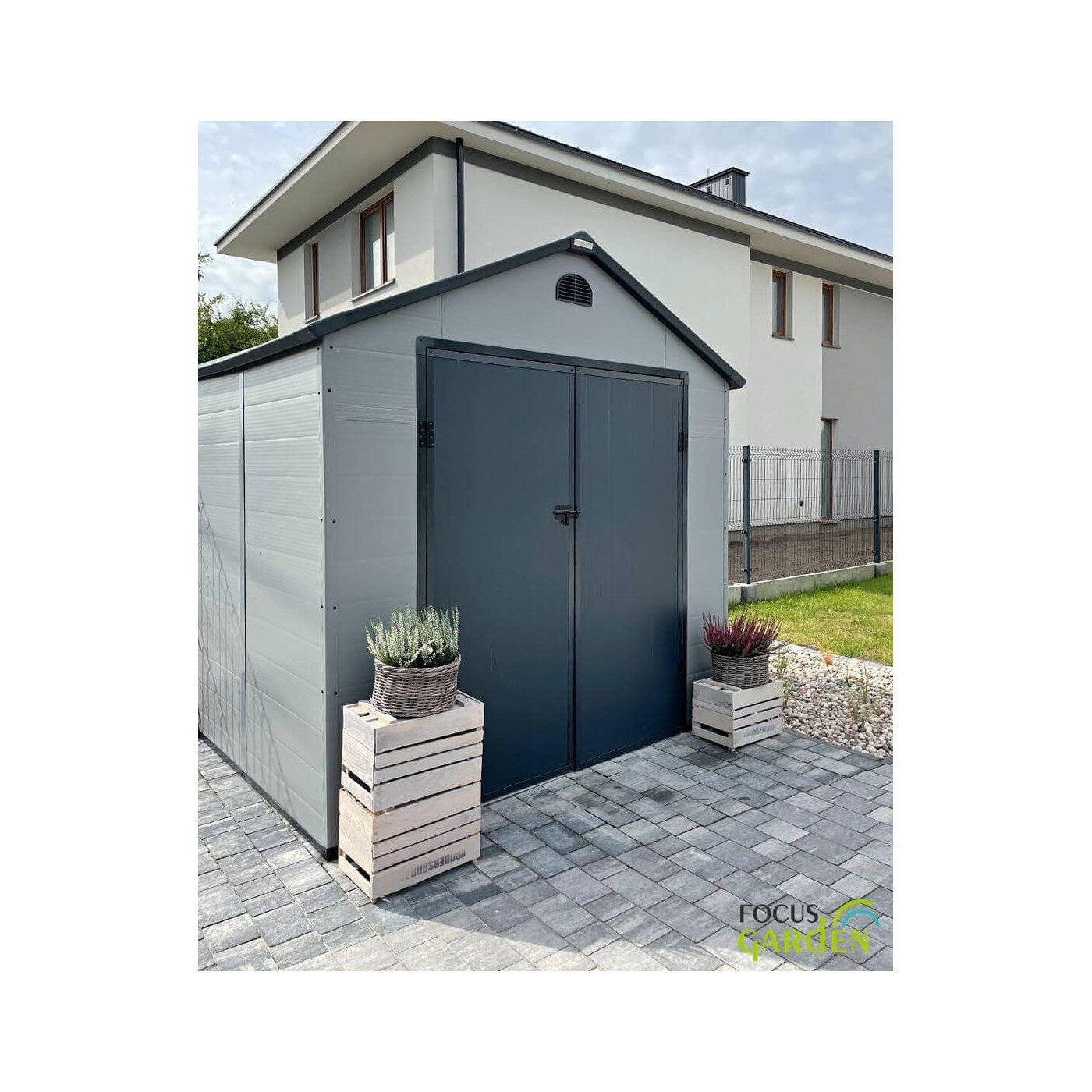 Aranżacja w ogrodzie domku narzędziowego Vermont 242x192cm od Hardmaister, kwiaty stoją przed domkiem, zabudowania za domkiem