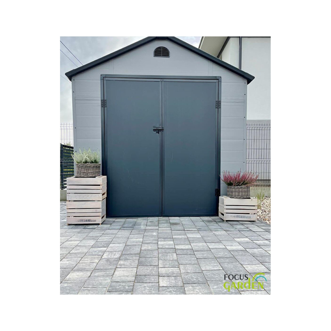 Przód domku ogrodowego Vermont 242x192cm od Hardmaister w kolorze Light Grey, w ogrodzie, kwiaty stoją przed domkiem