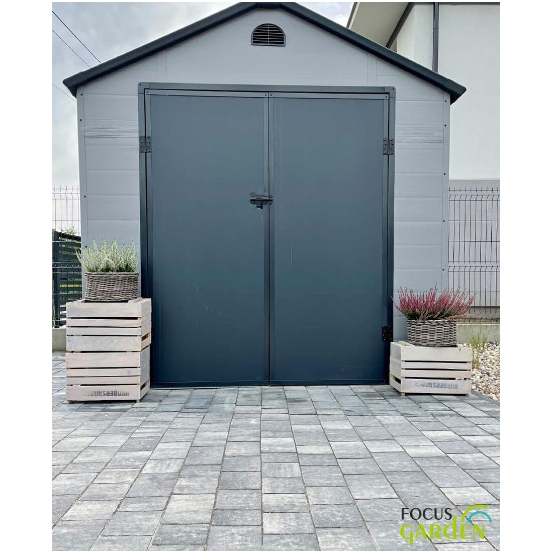 Przód domku ogrodowego Vermont 242x192cm od Hardmaister w kolorze Light Grey, w ogrodzie, kwiaty stoją przed domkiem