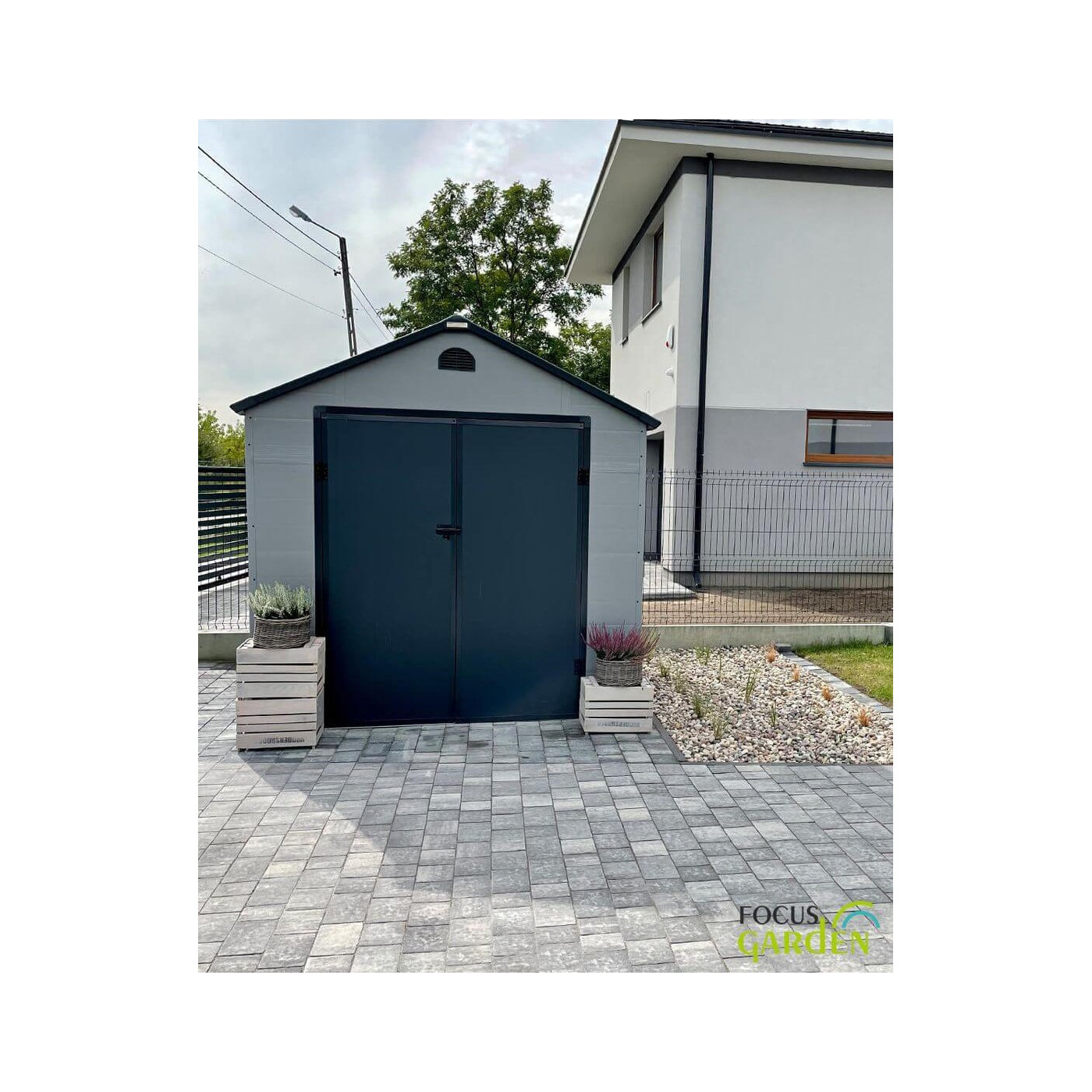 Aranżacja w ogrodzie domku narzędziowego Vermont 242x192cm od Hardmaister, kwiaty stoją przed domkiem, zabudowania za domkiem