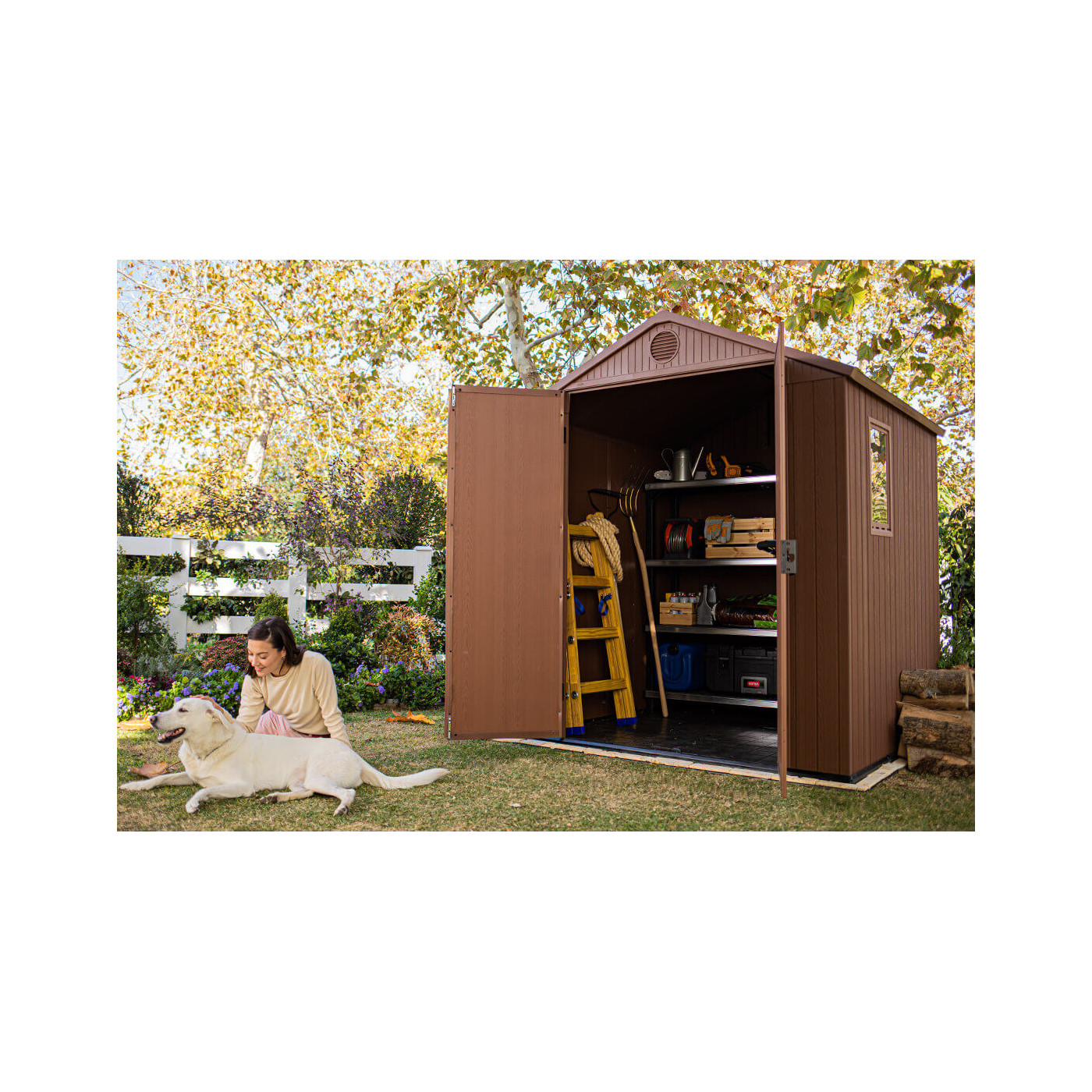 Aranżacja narzędziowni w ogrodzie, a obok niej kobieta bawiąca się z psem