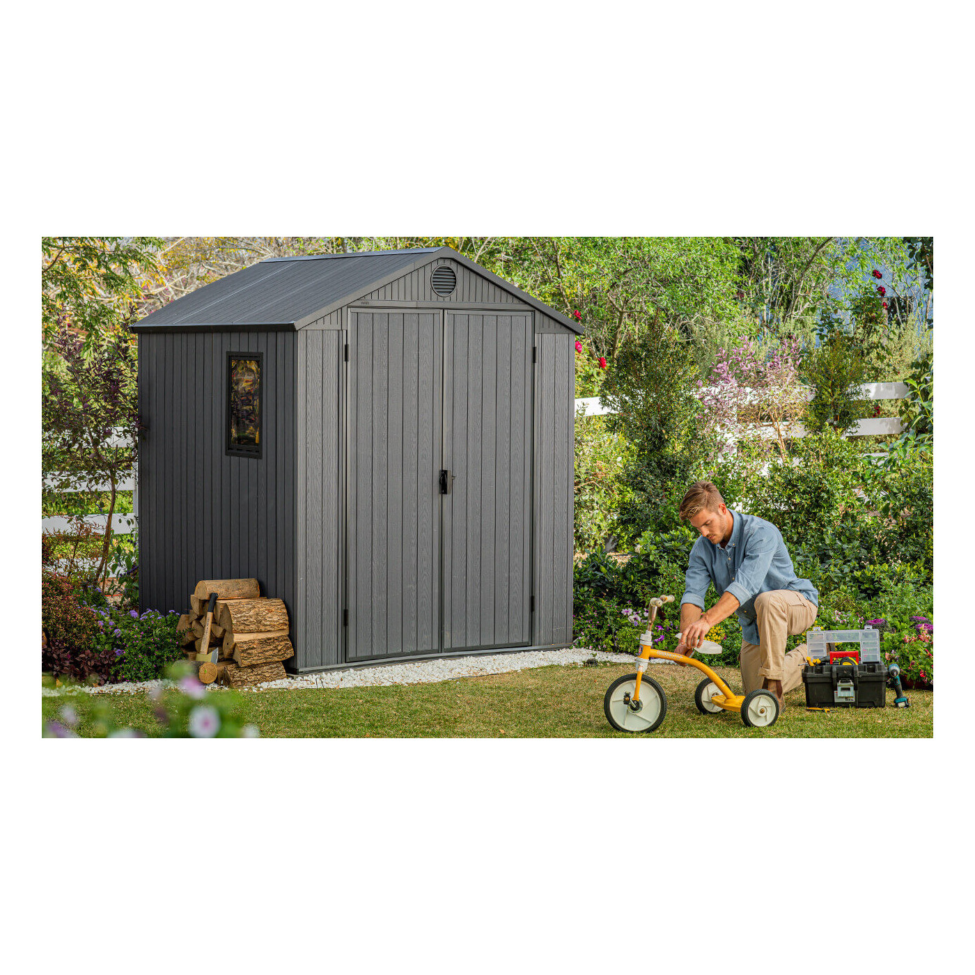 Aranżacja narzędziowni w ogrodzie, a obok niej mężczyzna naprawiający rowerek dziecięcy