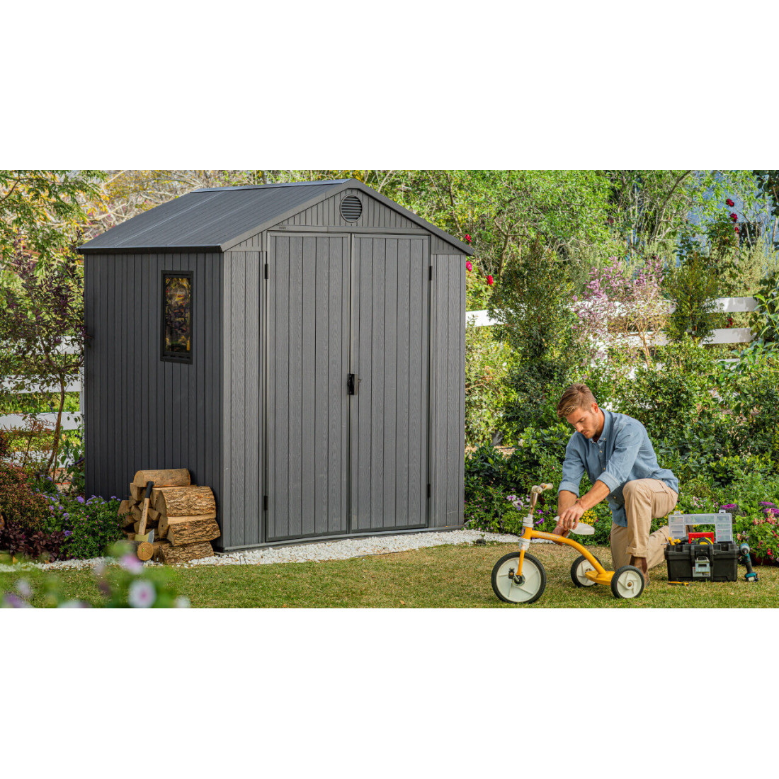 Aranżacja narzędziowni w ogrodzie, a obok niej mężczyzna naprawiający rowerek dziecięcy