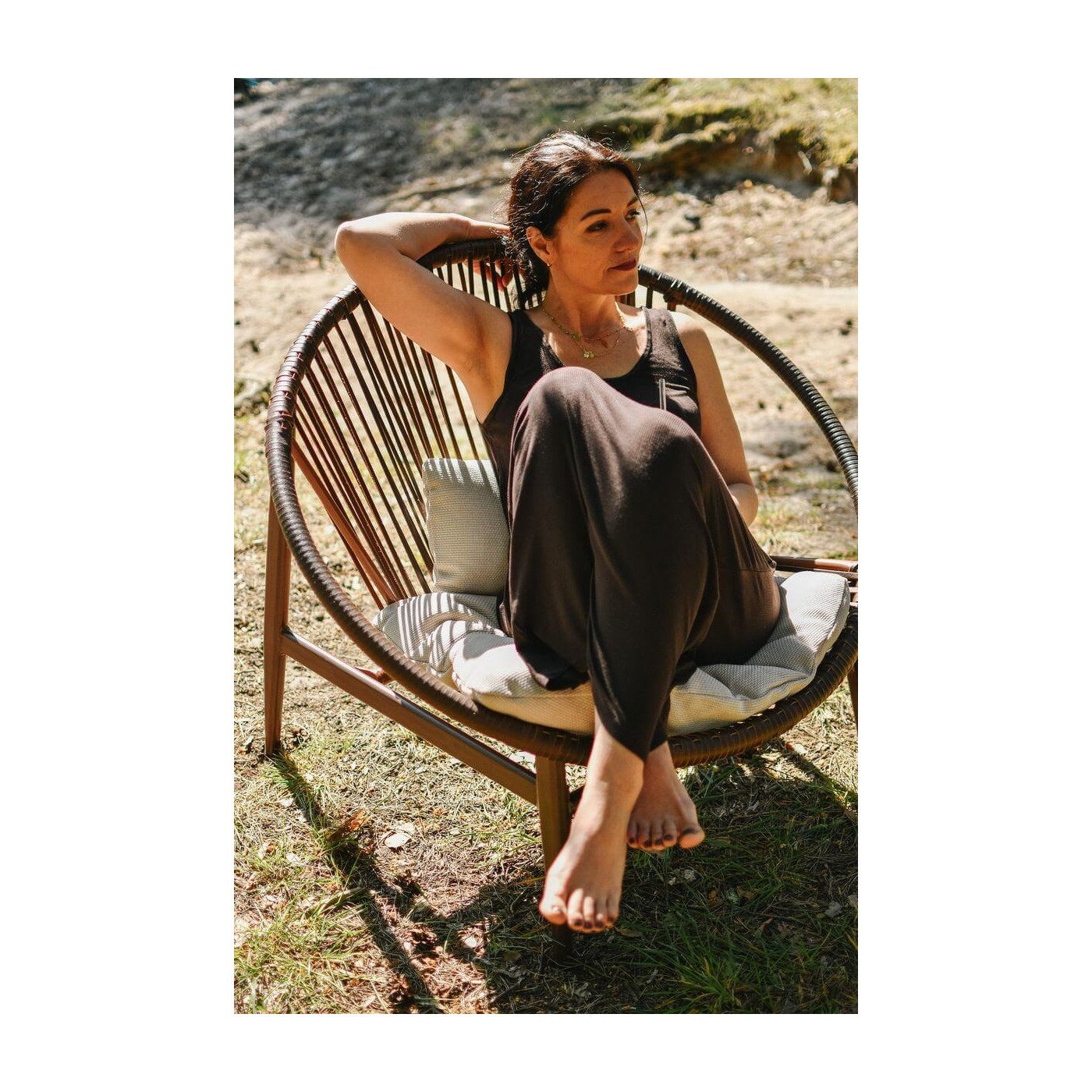 Kobieta siedząca na fotelu ogrodowym pośród drzew, korzystająca z telefonu