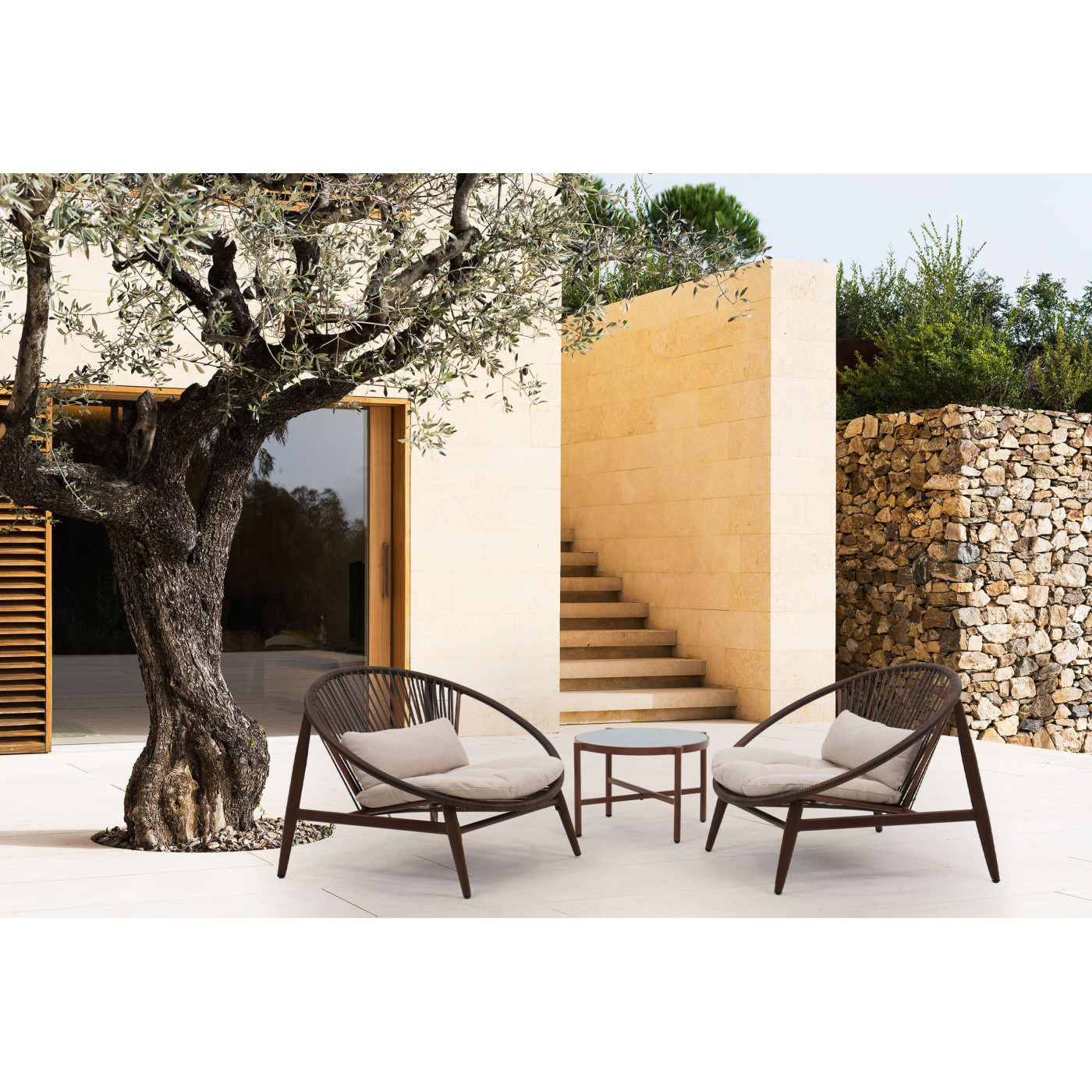 Aranżacja okrągłego stolika pośród drzew i trawy z ozdobnym wazonem