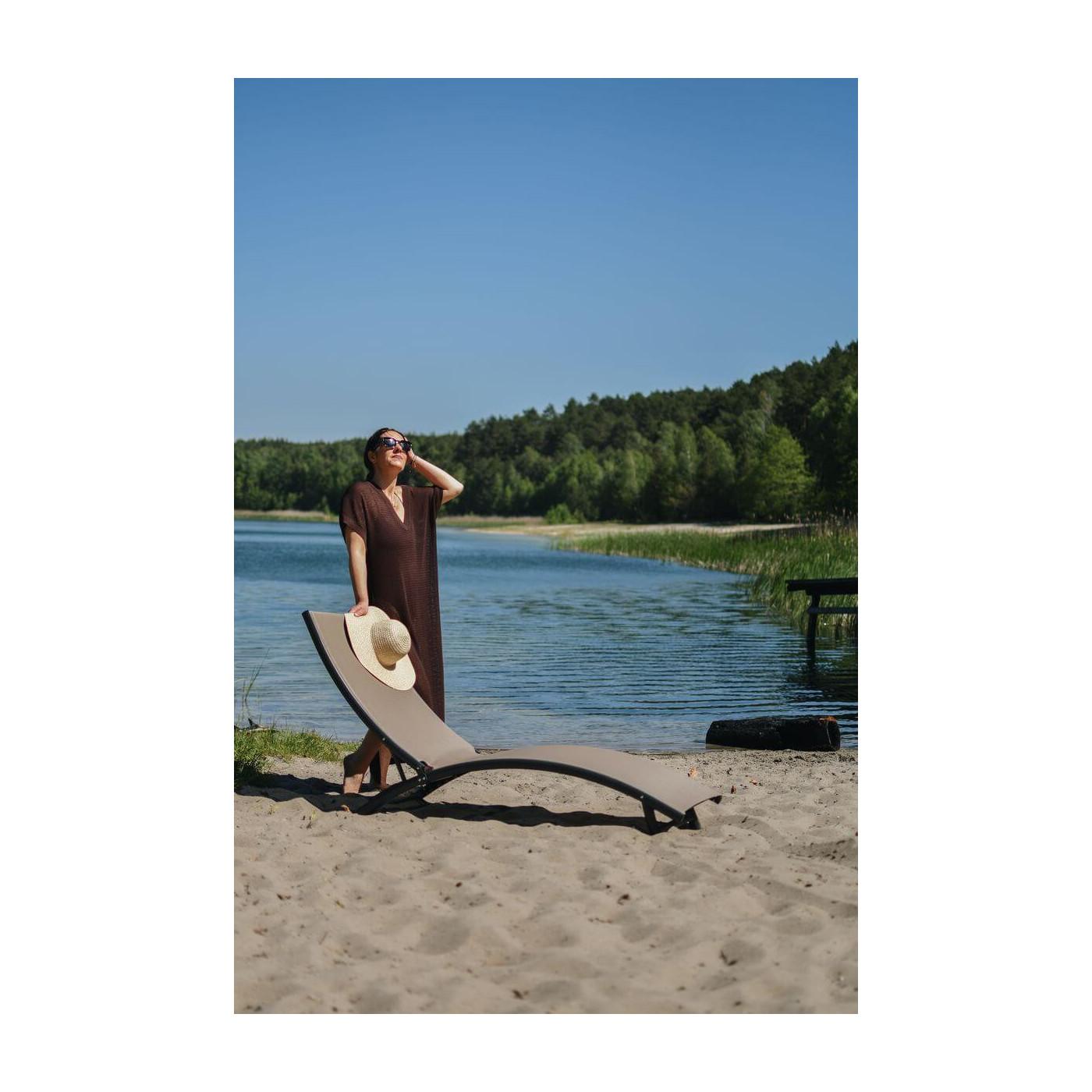Kobieta stojąca przy leżaku ogrodowym STAR przy jeziorze i zielonym otoczeniu drzew 