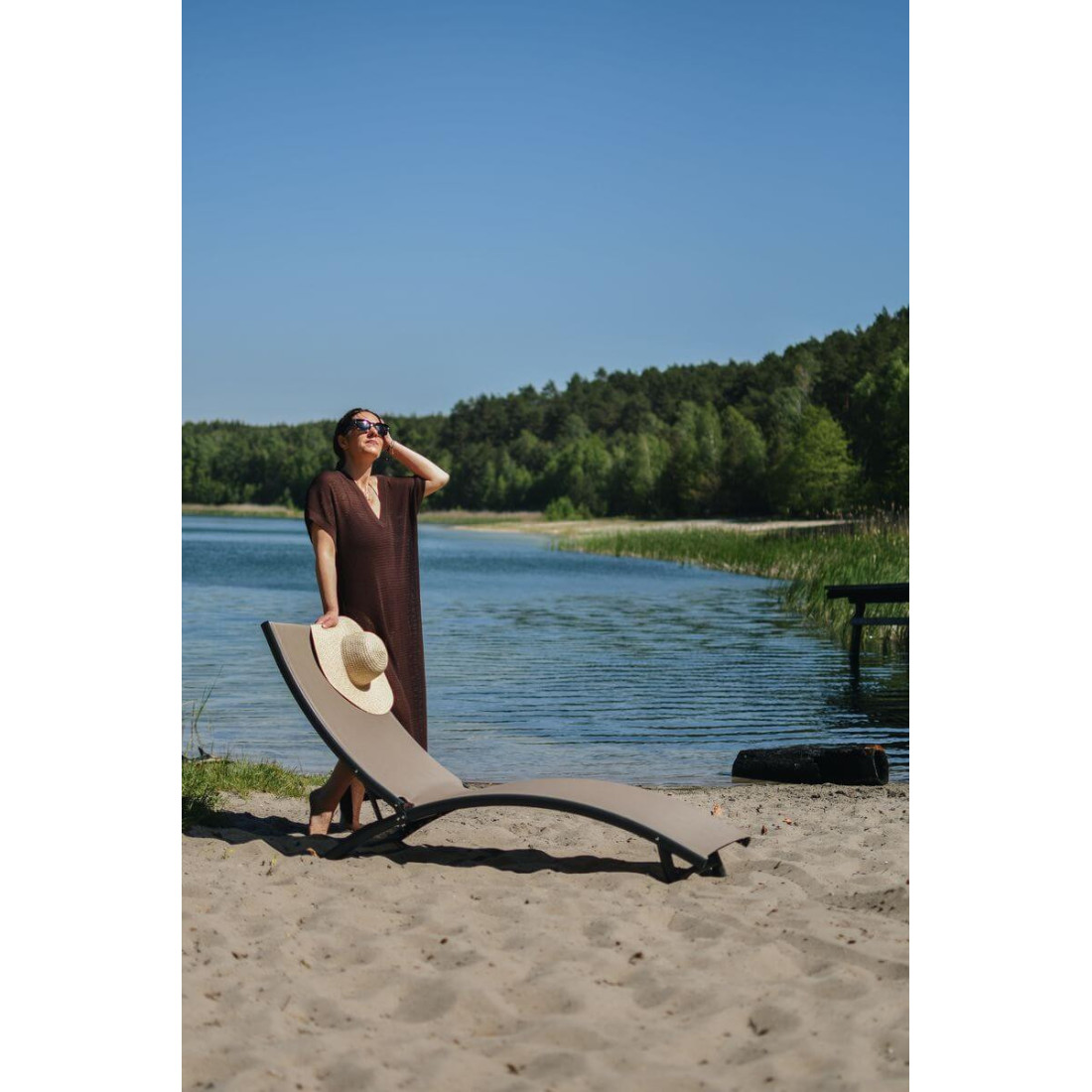 Kobieta stojąca przy leżaku ogrodowym STAR przy jeziorze i zielonym otoczeniu drzew 