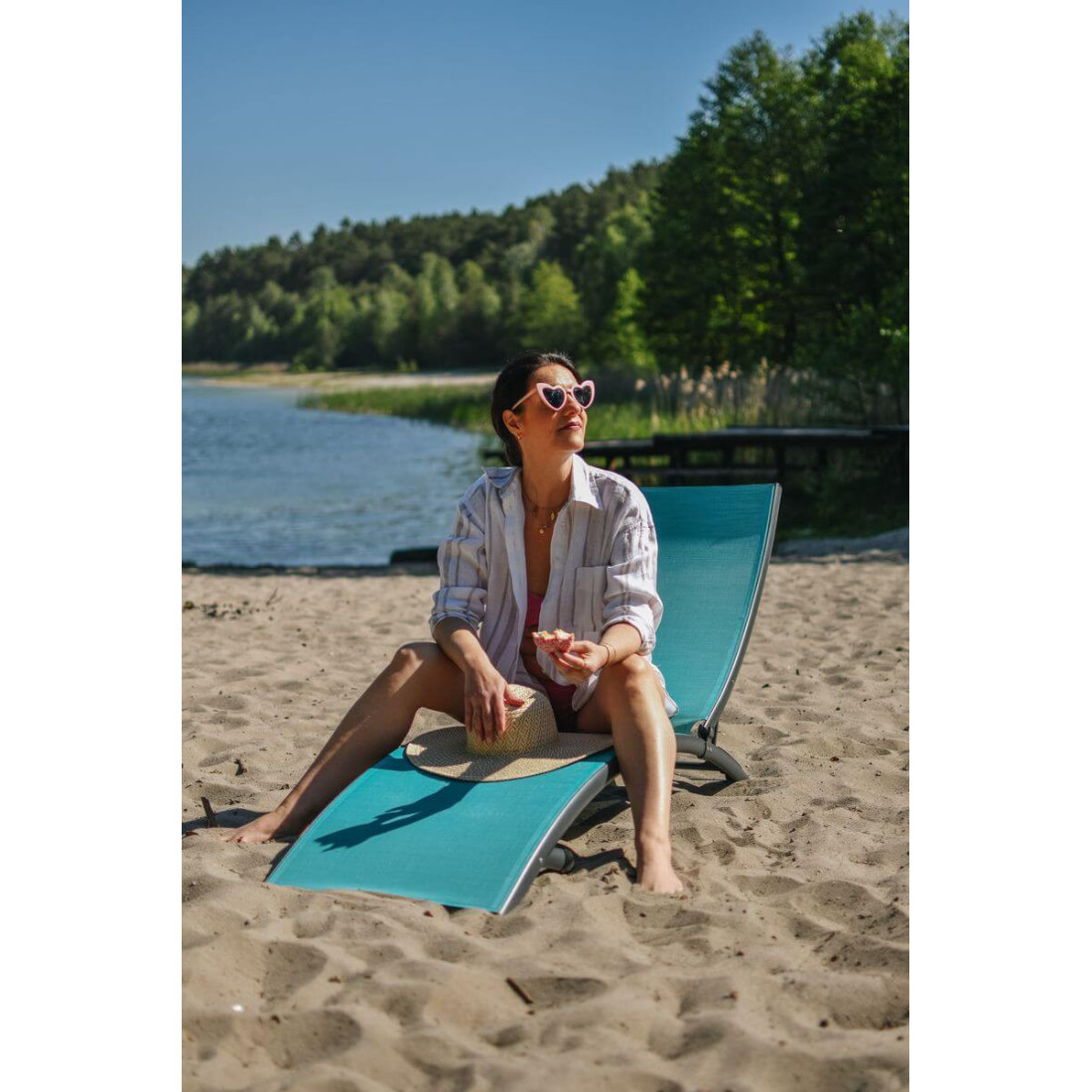 kobieta siedząca na niebieskim leżaku przy jeziorze wśród drzew