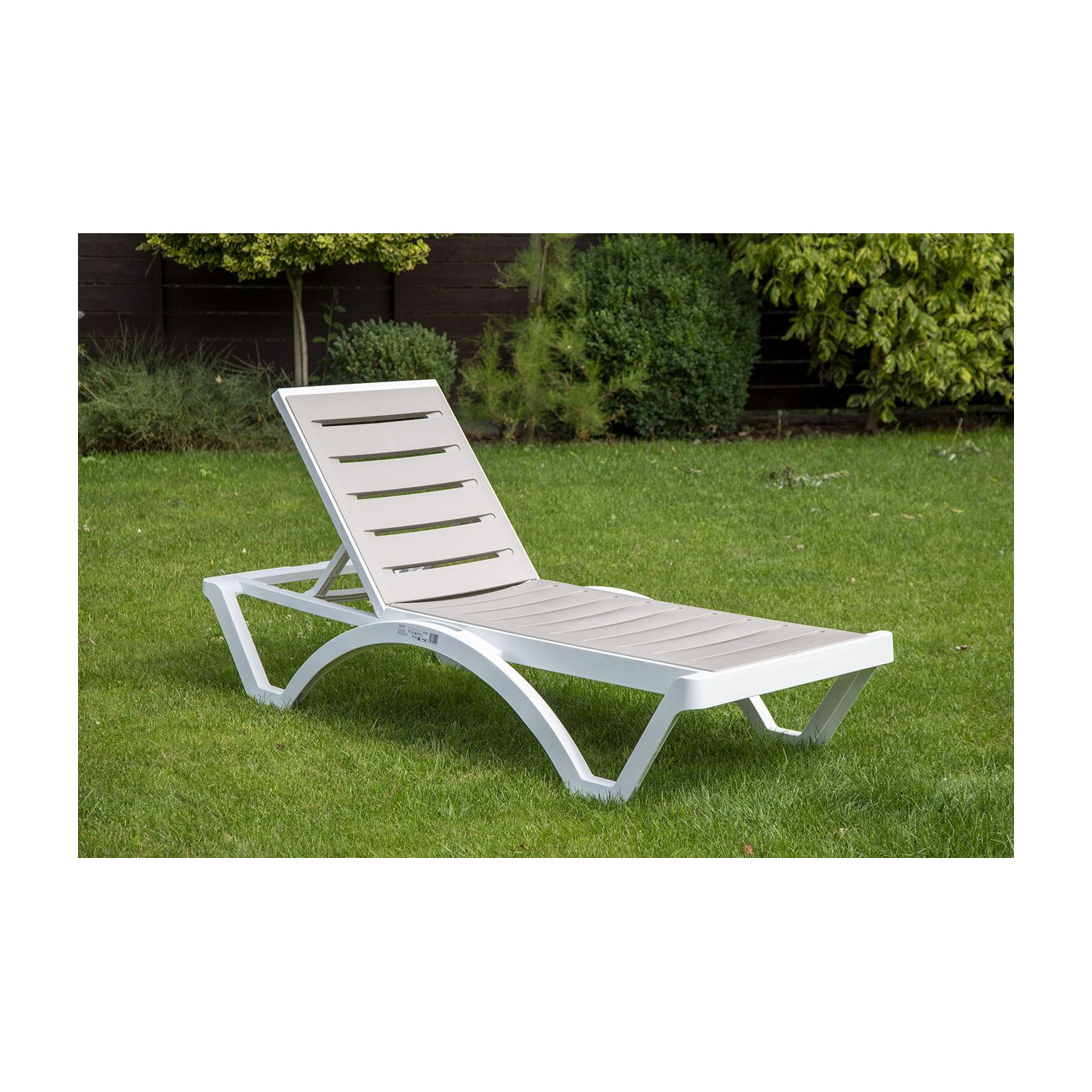 Szarobrązowy leżak lmbok z białą ramą na ogrodzie 