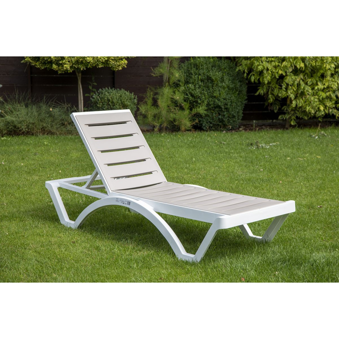 Szarobrązowy leżak lmbok z białą ramą na ogrodzie 