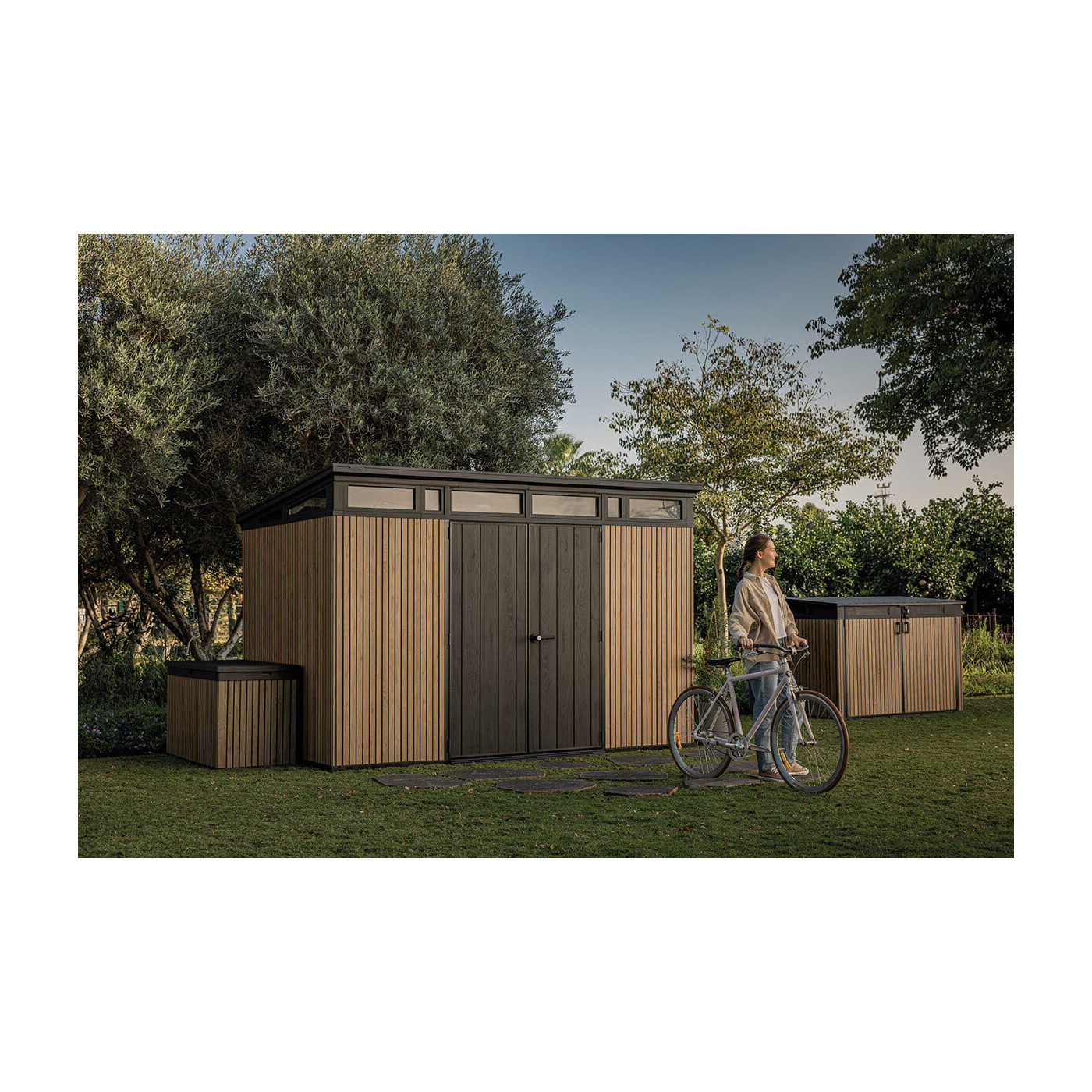 Aranżacja szopy na narzędzia w ogrodzie, obok niej kobieta z rowerem