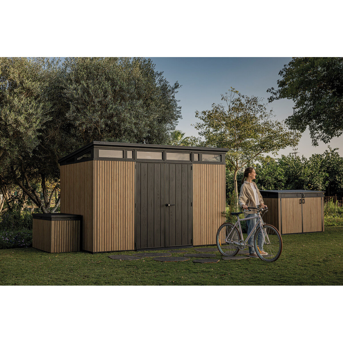 Aranżacja szopy na narzędzia w ogrodzie, obok niej kobieta z rowerem