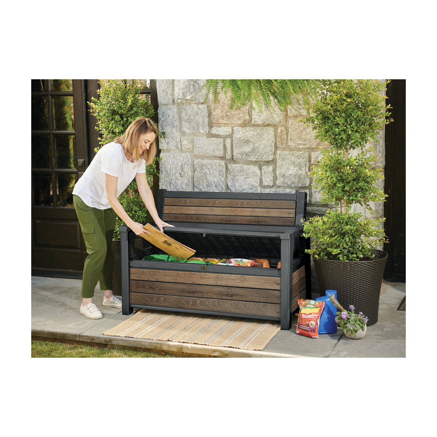 Kobieta wkładająca papierowe opakowanie do skrzyni ogrodowej, która pełni również funkcję ławki ogrodowej