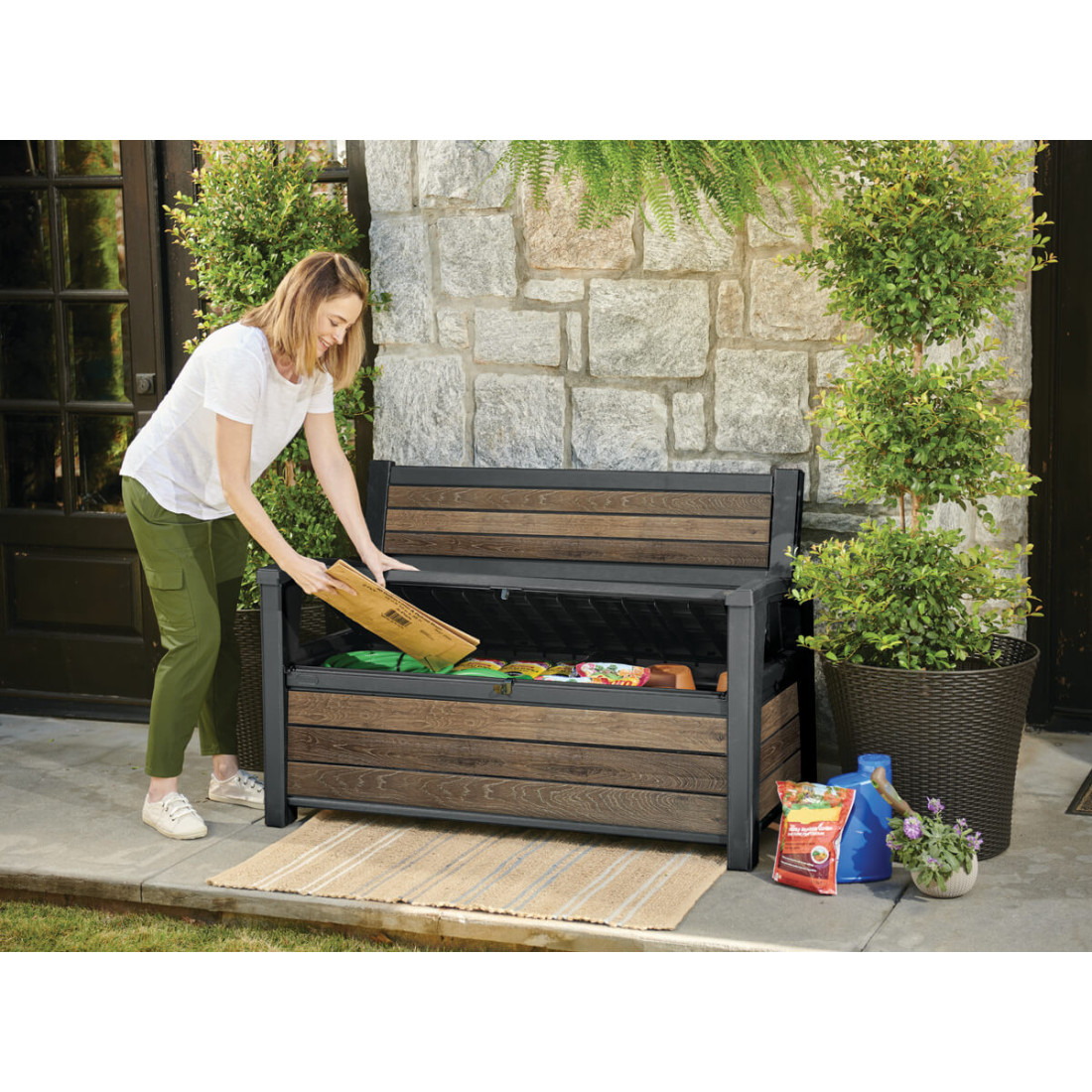 Kobieta wkładająca papierowe opakowanie do skrzyni ogrodowej, która pełni również funkcję ławki ogrodowej