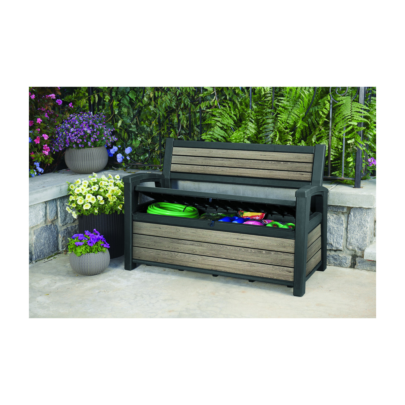 Otwarta skrzynia ogrodowa wypełniona wężem ogrodowym, ziemią oraz kolorowymi pudełkami