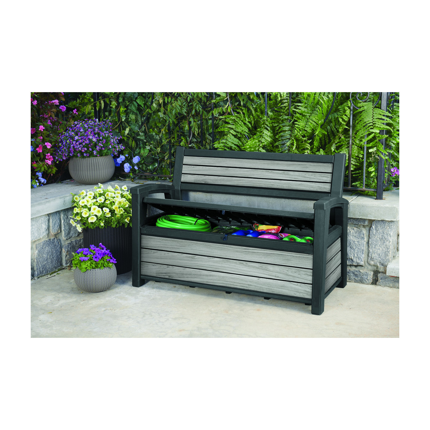 Otwarta skrzynia ogrodowa w ławce ogrodowej, w której znajdują się akcesoria ogrodowe