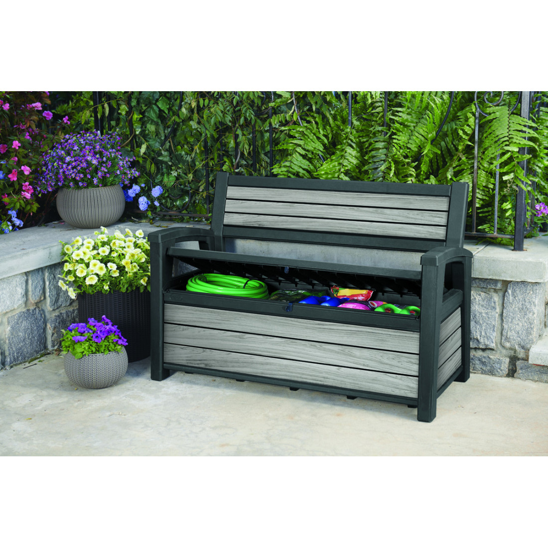 Otwarta skrzynia ogrodowa w ławce ogrodowej, w której znajdują się akcesoria ogrodowe