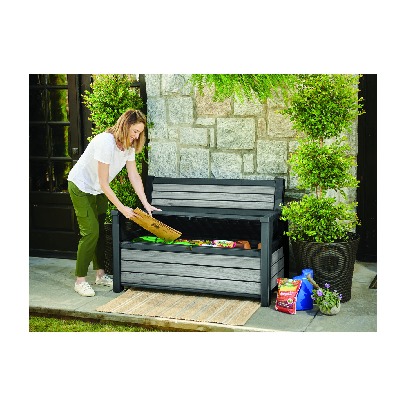 Kobieta schyla się nad skrzynią ogrodowej i z uśmiechem wkłada do niej karton