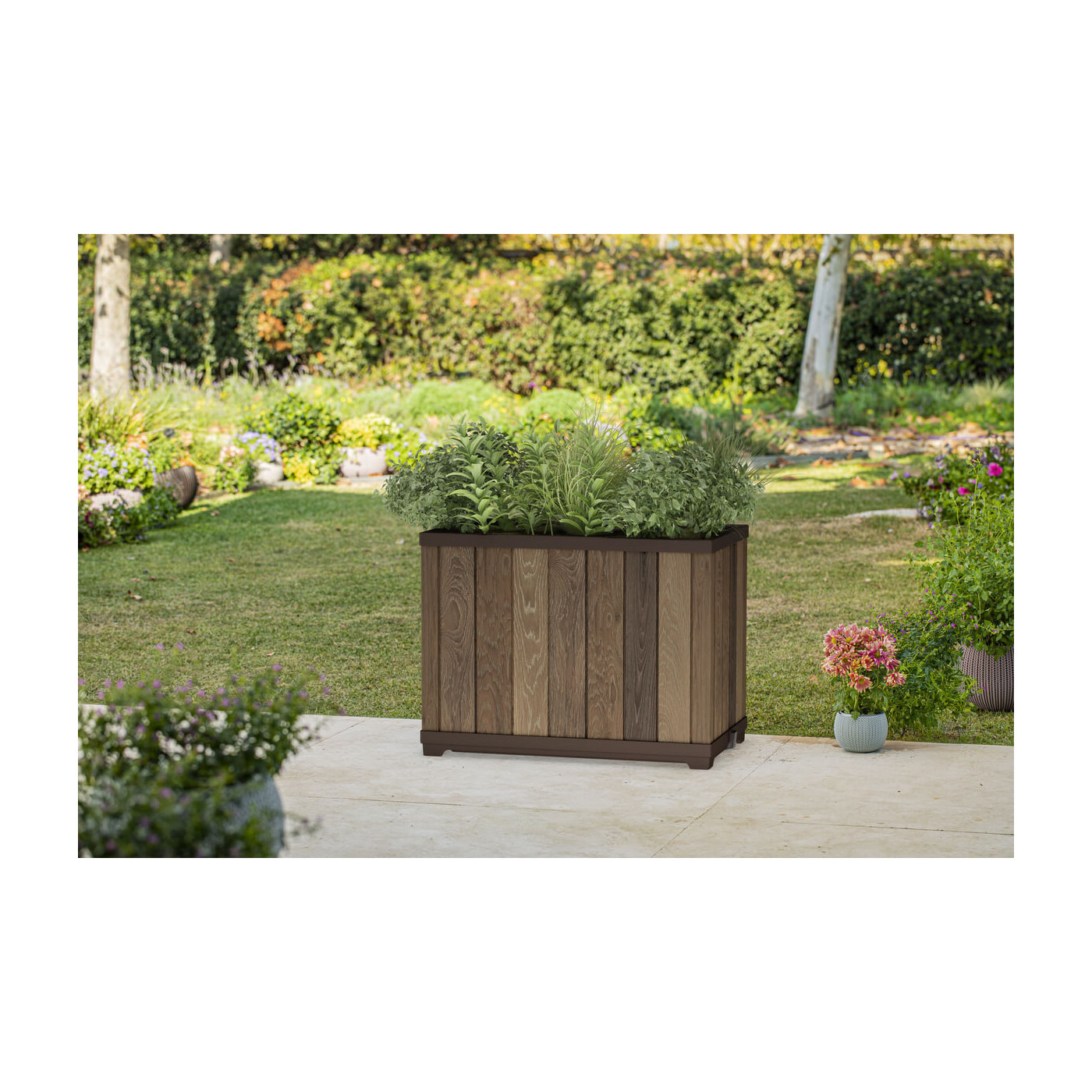 Duża, prostokątna donica w przydomowym ogrodzie w otoczeniu drzew, krzewów i kwiatów