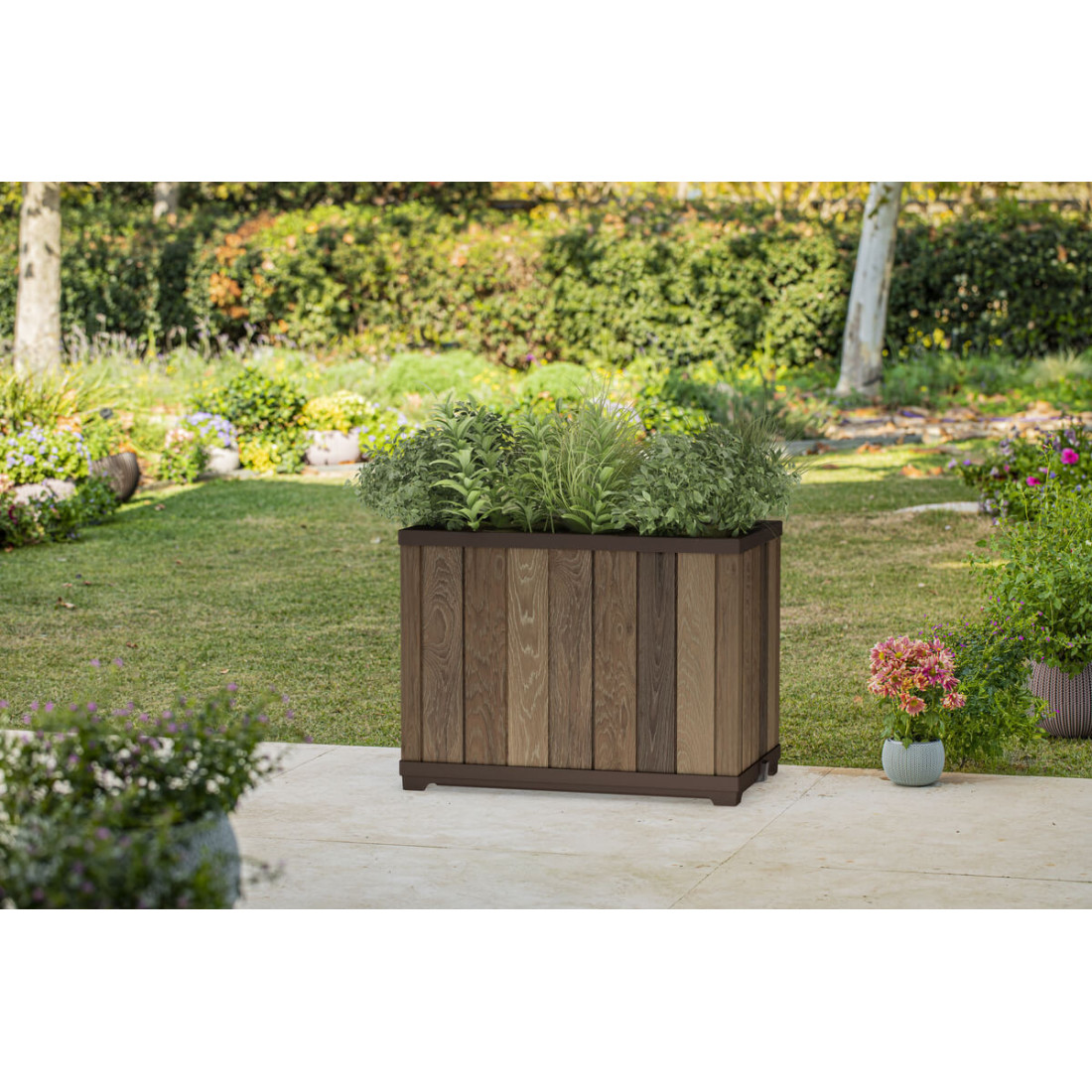 Duża, prostokątna donica w przydomowym ogrodzie w otoczeniu drzew, krzewów i kwiatów