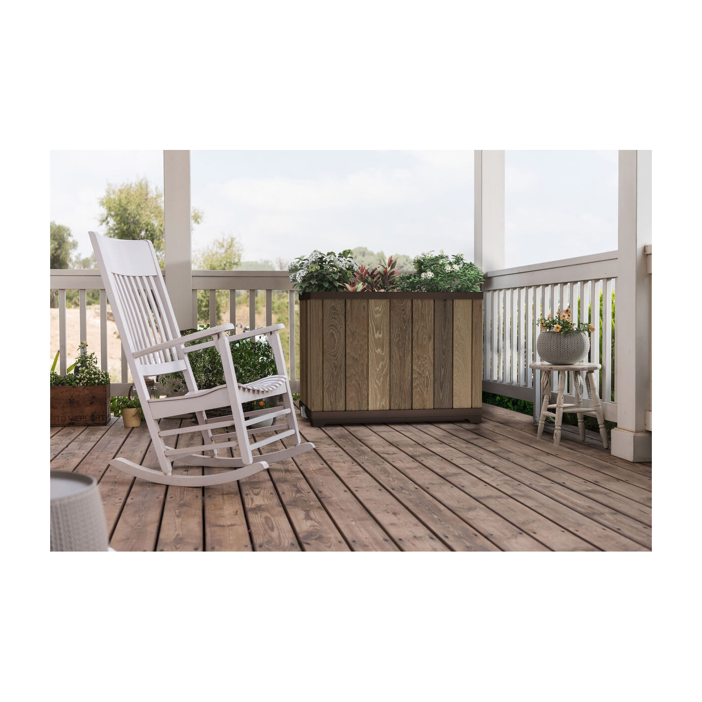 Brązowa doniczka wypełniona kwiatami na tarasie przy białym, bujanym fotelu