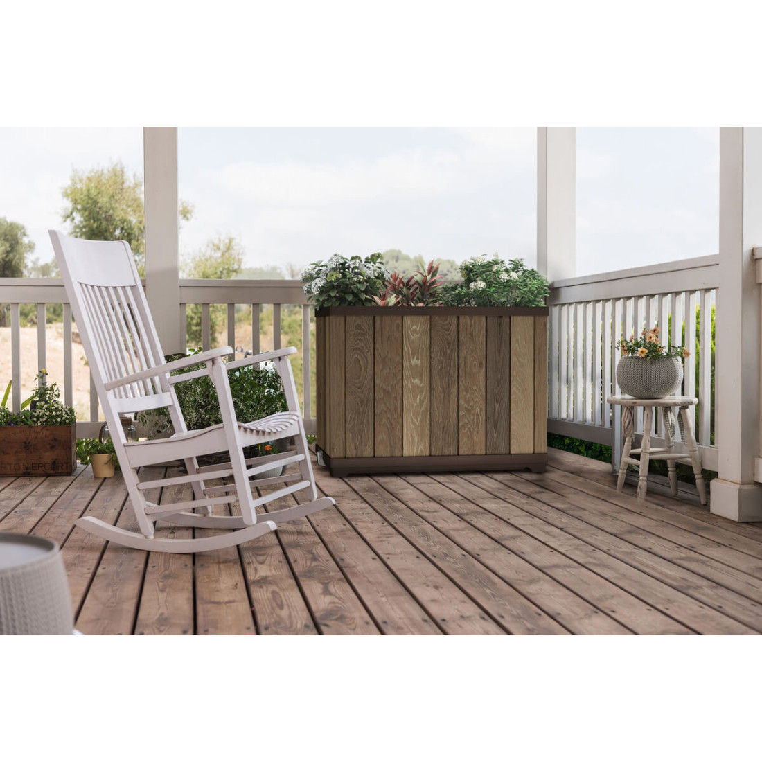 Brązowa doniczka wypełniona kwiatami na tarasie przy białym, bujanym fotelu