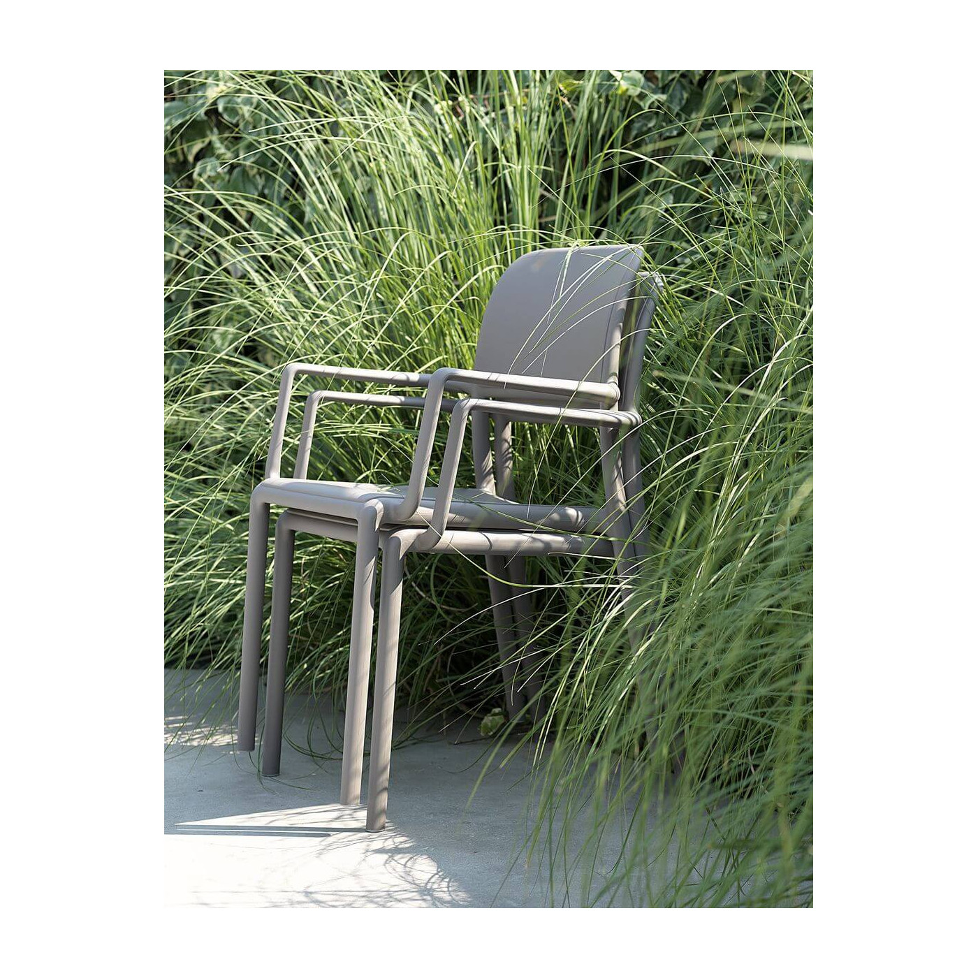 Krzesła RIVA Agave Nardi ustawione jedno na drugim wśród wysokich ozdobnych traw – przykład funkcjonalnego przechowywania.