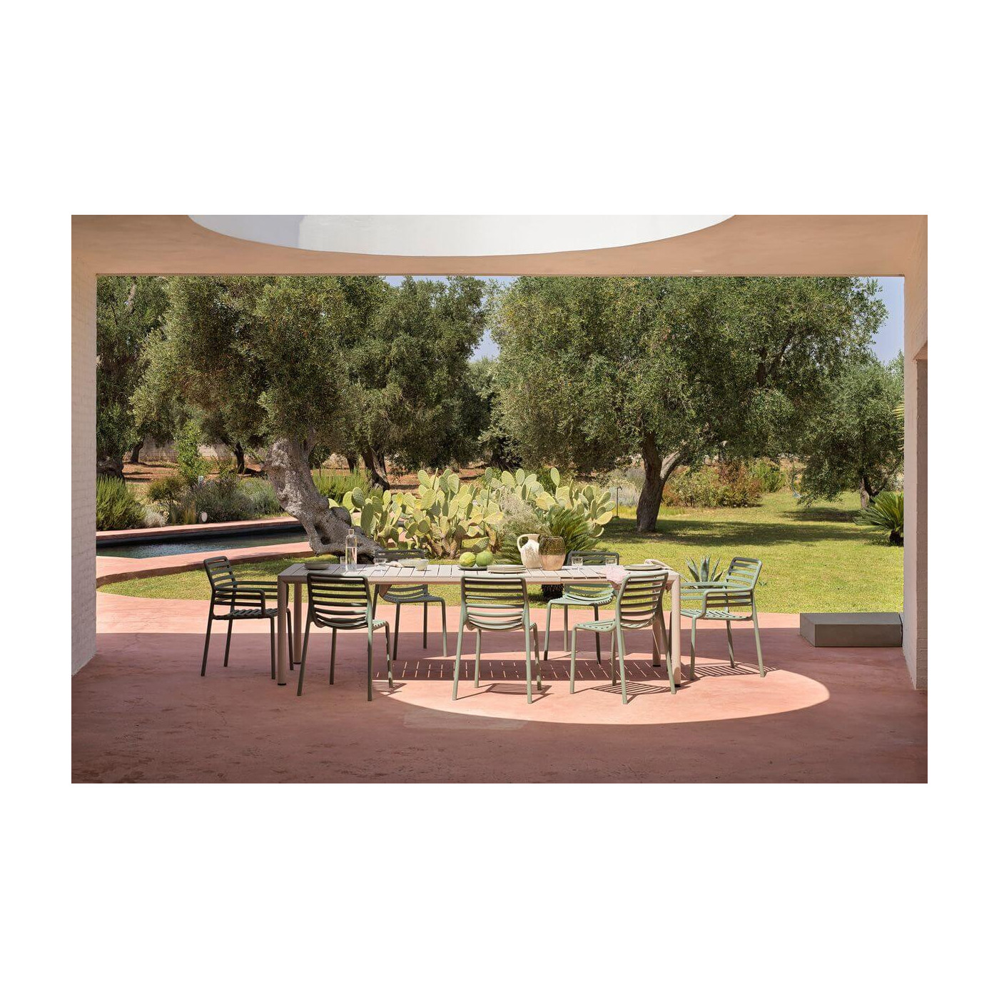 Rozłożony stół TEVERE 210 Corda na przestronnym tarasie, z widokiem na drzewa i ogród